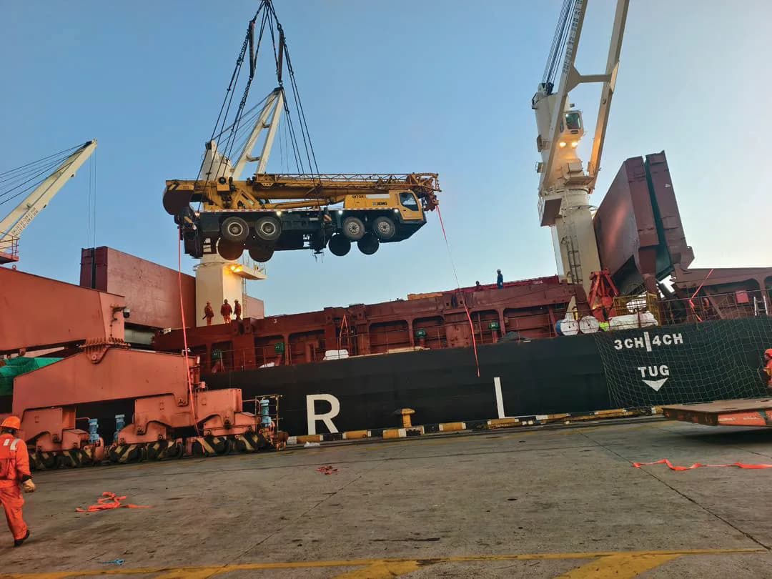 Heavy mobile crane being lifted onto a cargo vessel at port