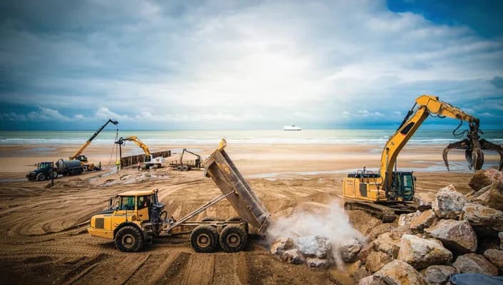 Articulated dump truck and excavator carrying out earthmoving on a coastal site